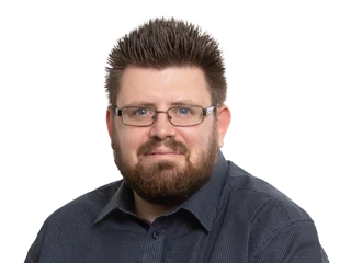 Portrait of a man with short dark hair, beard, and glasses wearing a dark blue button-up shirt, looking at the camera.